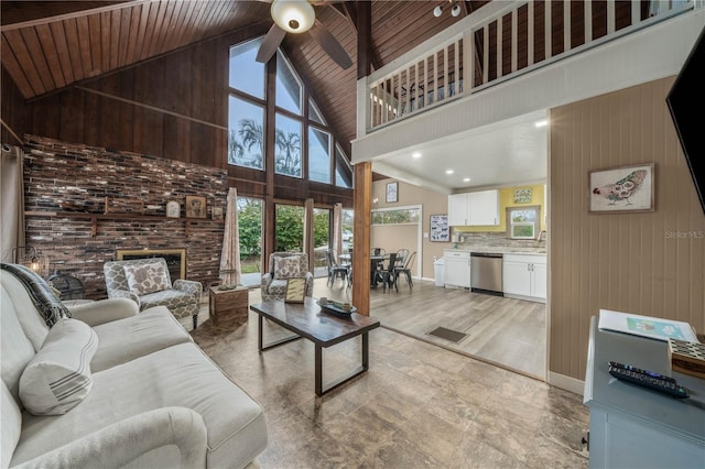 living room with wooden ceiling, ceiling fan, wood walls, a fireplace, and high vaulted ceiling