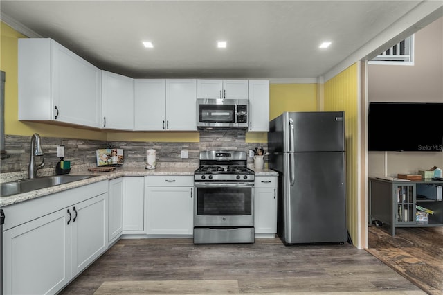 kitchen with wood finished floors, a sink, white cabinetry, appliances with stainless steel finishes, and tasteful backsplash