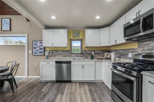 kitchen with wood finished floors, a sink, white cabinets, appliances with stainless steel finishes, and backsplash