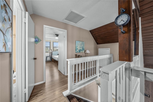 hallway with attic access, wood finished floors, vaulted ceiling, a textured ceiling, and an upstairs landing