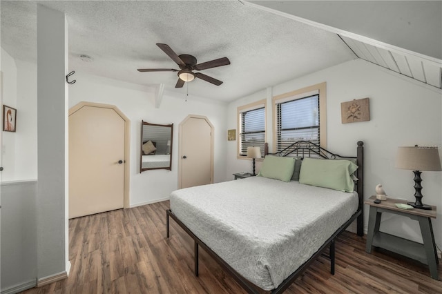 bedroom with a textured ceiling, arched walkways, wood finished floors, a ceiling fan, and vaulted ceiling