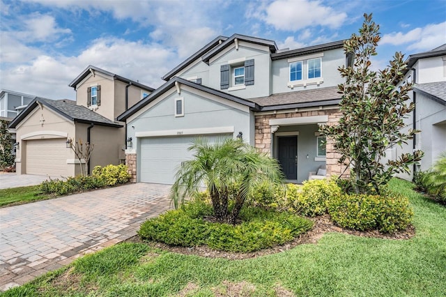 view of front of property with a garage, stone siding, decorative driveway, and stucco siding