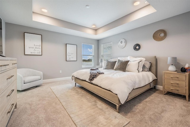 bedroom featuring baseboards, a raised ceiling, and light colored carpet