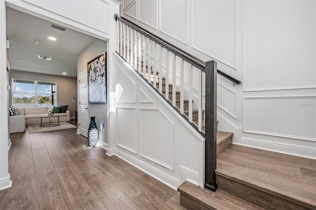 stairs featuring baseboards, visible vents, wood finished floors, a decorative wall, and recessed lighting