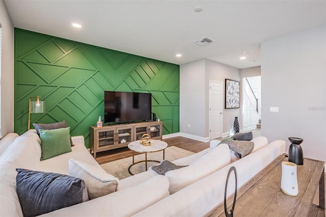 living room with recessed lighting, visible vents, an accent wall, wood finished floors, and baseboards