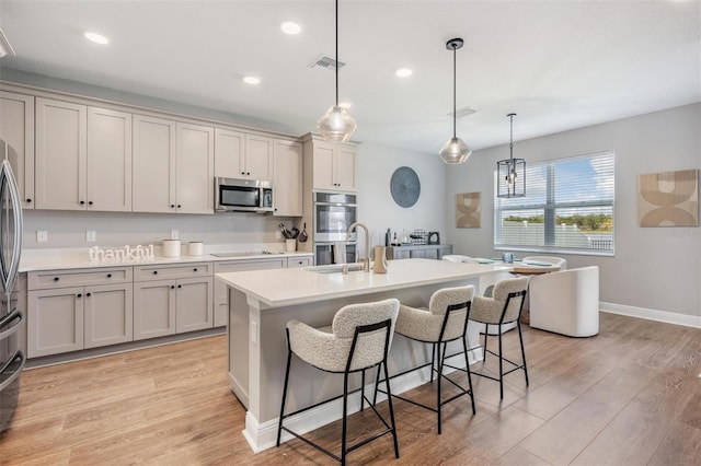 kitchen with stainless steel appliances, light countertops, hanging light fixtures, a sink, and an island with sink