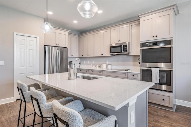 kitchen featuring appliances with stainless steel finishes, a kitchen island with sink, a sink, and decorative light fixtures