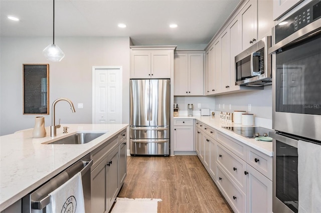 kitchen featuring wood finished floors, a sink, hanging light fixtures, appliances with stainless steel finishes, and light stone countertops