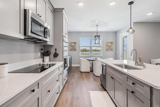 kitchen featuring appliances with stainless steel finishes, light stone countertops, gray cabinets, pendant lighting, and a sink