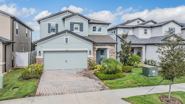 view of front facade with a garage, stone siding, fence, decorative driveway, and stucco siding