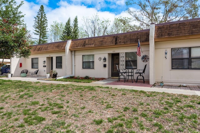 back of property featuring a patio area, stucco siding, roof with shingles, and mansard roof