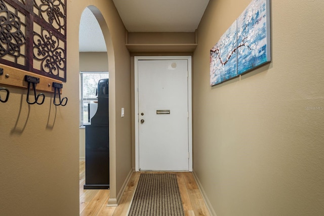 entryway featuring arched walkways, light wood-type flooring, and baseboards