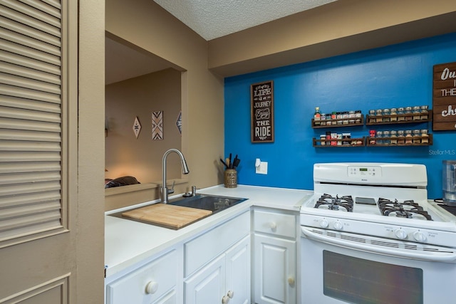 kitchen featuring a textured ceiling, a sink, white cabinets, light countertops, and gas range gas stove