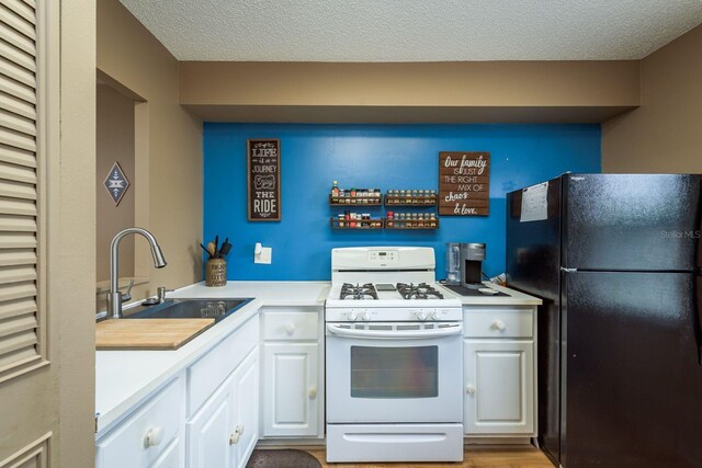 kitchen with white range with gas stovetop, freestanding refrigerator, light countertops, white cabinetry, and a sink