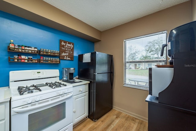 kitchen with light wood-style flooring, freestanding refrigerator, white gas range, light countertops, and white cabinetry