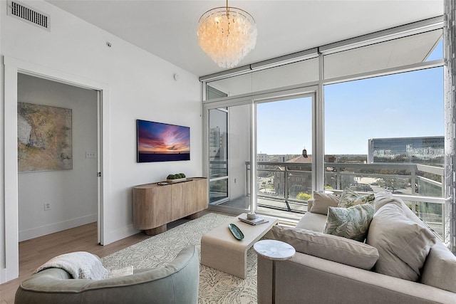 living room featuring baseboards, visible vents, light wood-style flooring, expansive windows, and a notable chandelier