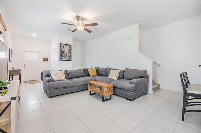 living area featuring visible vents, light tile patterned flooring, ceiling fan, and stairway