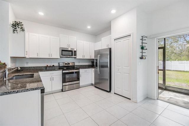 kitchen featuring light tile patterned floors, a sink, white cabinets, appliances with stainless steel finishes, and dark stone countertops