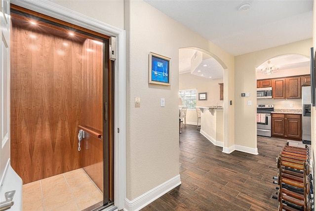 corridor featuring arched walkways, dark wood-style flooring, elevator, and baseboards