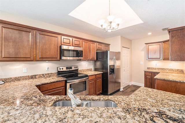 kitchen with stainless steel appliances, brown cabinets, a sink, and light stone countertops