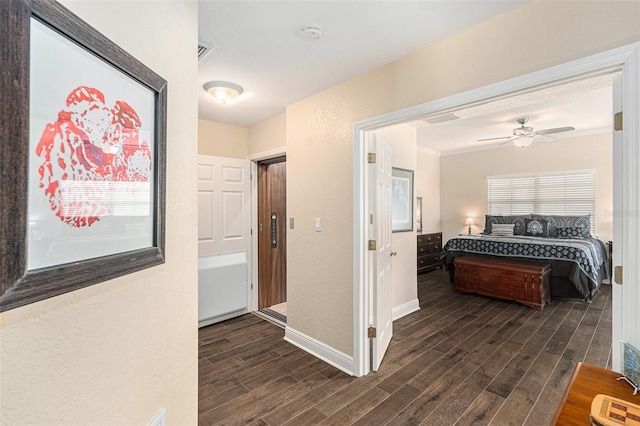 hall featuring crown molding, dark wood finished floors, visible vents, a textured wall, and baseboards