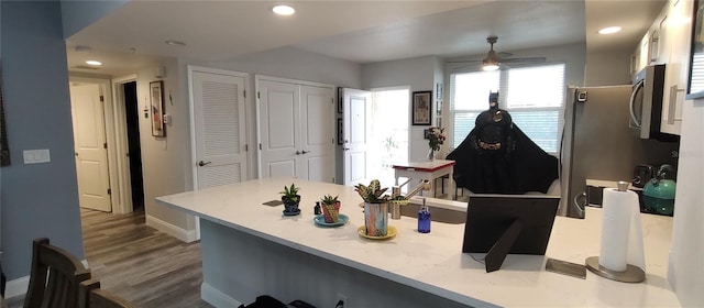 interior space with a breakfast bar, light countertops, stainless steel microwave, wood finished floors, and a peninsula