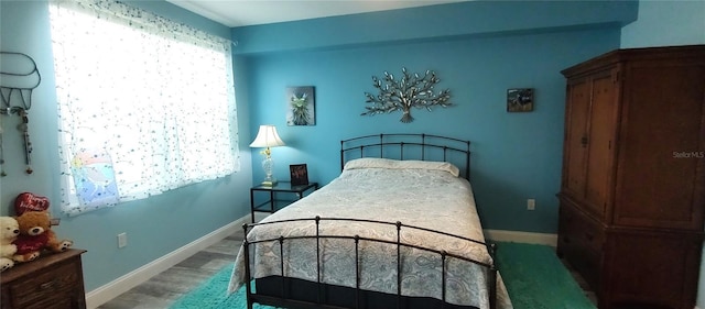 bedroom with multiple windows, wood finished floors, and baseboards