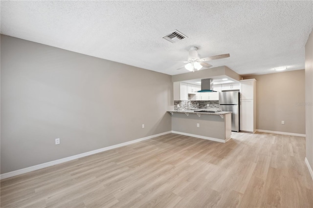 kitchen with island range hood, a peninsula, visible vents, white cabinets, and freestanding refrigerator