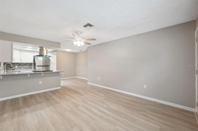 unfurnished living room with visible vents, light wood-style floors, a ceiling fan, a sink, and baseboards