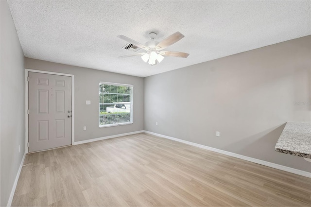 spare room featuring light wood finished floors, visible vents, baseboards, and a textured ceiling