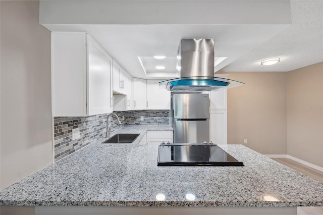 kitchen featuring white cabinets, a peninsula, freestanding refrigerator, and island range hood