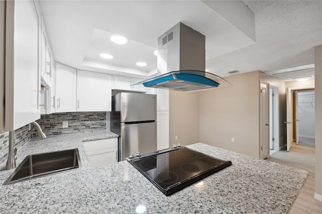 kitchen with a raised ceiling, island exhaust hood, freestanding refrigerator, and white cabinets