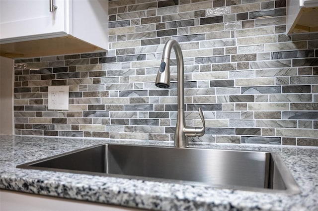 details with tasteful backsplash, light stone counters, white cabinets, and a sink