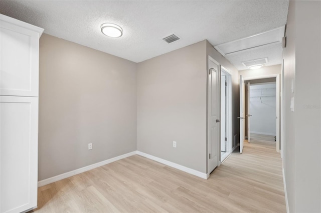 unfurnished room featuring a textured ceiling, light wood finished floors, visible vents, and baseboards