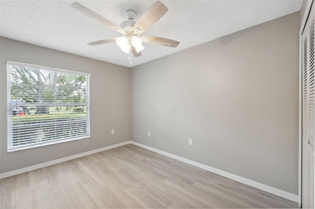 empty room with a textured ceiling, ceiling fan, light wood finished floors, and baseboards