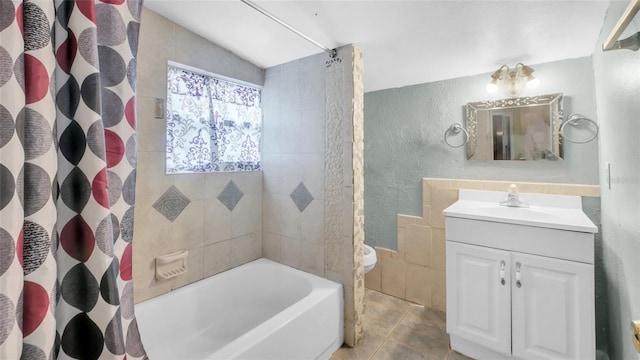 full bathroom featuring toilet, a textured wall, shower / tub combo with curtain, and vanity