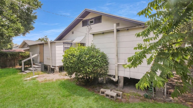 view of property exterior featuring a lawn, fence, and entry steps