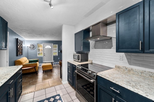 kitchen featuring tasteful backsplash, baseboards, wall chimney exhaust hood, blue cabinets, and stainless steel appliances