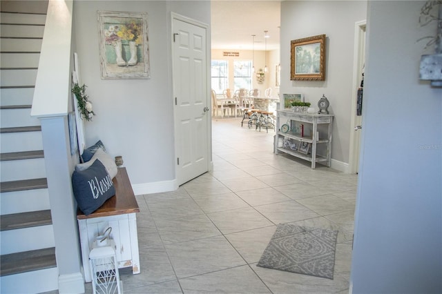 hallway featuring stairs, light tile patterned floors, and baseboards