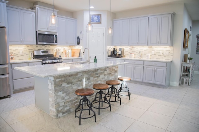 kitchen with appliances with stainless steel finishes, light stone counters, decorative light fixtures, a kitchen island with sink, and a sink