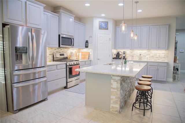 kitchen featuring light stone counters, stainless steel appliances, a sink, a kitchen breakfast bar, and a center island with sink