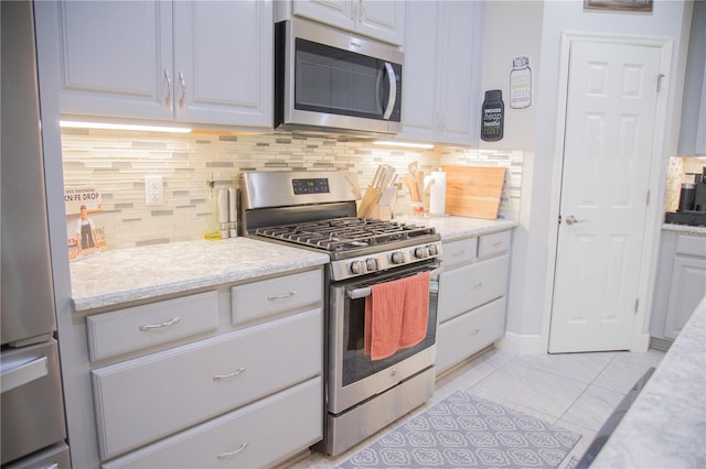 kitchen featuring stainless steel appliances, white cabinetry, decorative backsplash, and light stone countertops