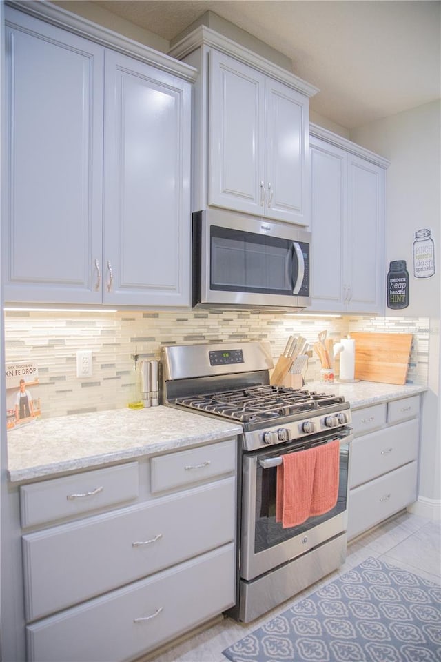 kitchen featuring appliances with stainless steel finishes, light tile patterned flooring, decorative backsplash, and white cabinetry