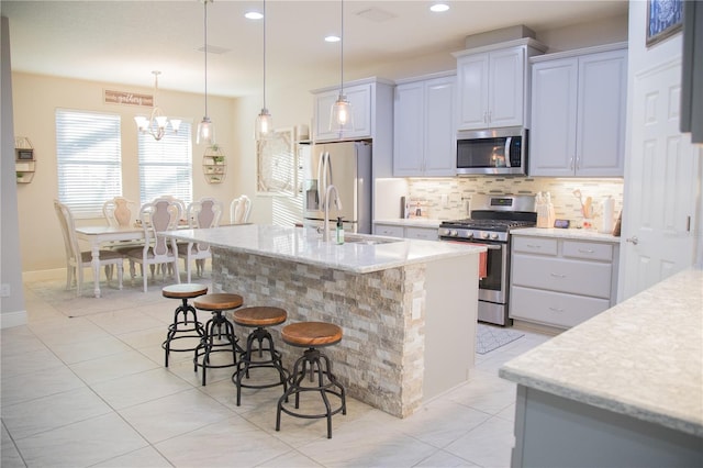 kitchen featuring light stone counters, a kitchen island with sink, stainless steel appliances, a sink, and hanging light fixtures