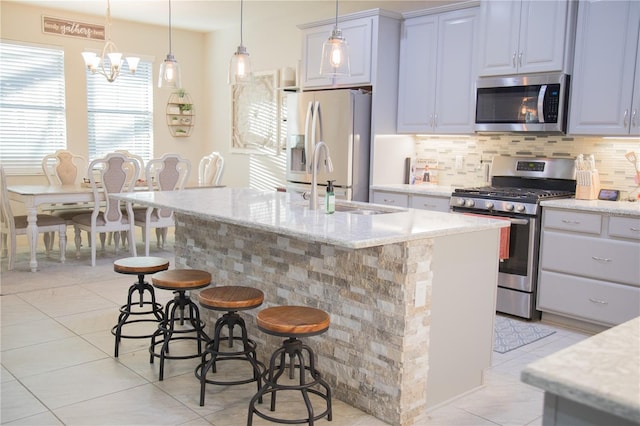 kitchen with pendant lighting, a center island with sink, stainless steel appliances, tasteful backsplash, and light stone countertops