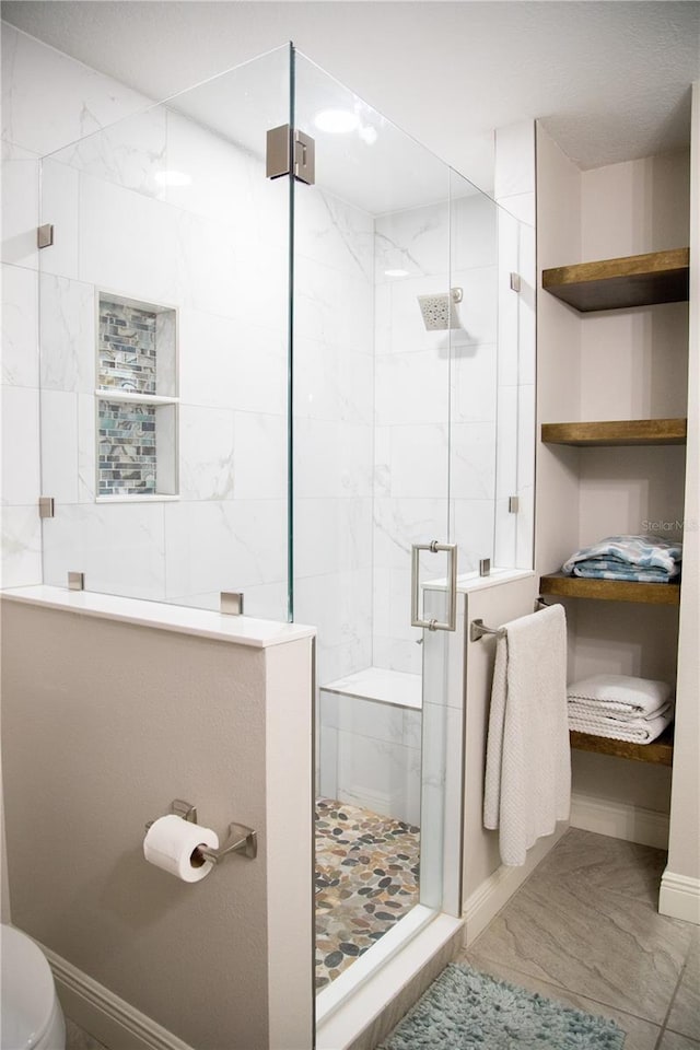 bathroom with marble finish floor, baseboards, a shower stall, and toilet