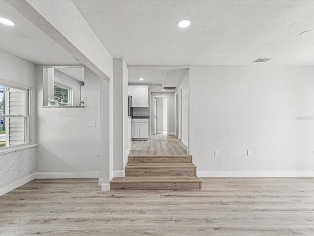 hall with light wood-style floors, baseboards, visible vents, and a textured ceiling