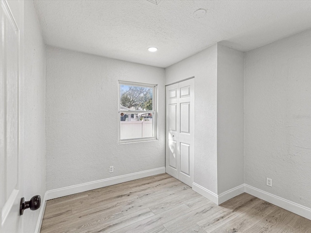 spare room featuring a textured wall, light wood finished floors, and baseboards