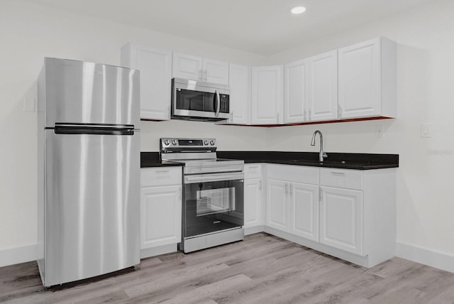 kitchen featuring baseboards, white cabinets, appliances with stainless steel finishes, light wood-type flooring, and a sink