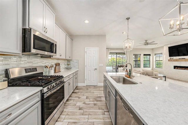 kitchen with stainless steel appliances, a sink, open floor plan, decorative backsplash, and pendant lighting